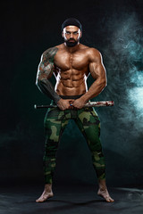 Strong and fit man bodybuilder with baseball bat shows abdominal muscles under a t-shirt. Sporty...