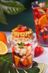 Fototapeta na wymiar Red wine fresh sangria or punch with fruits, mint leaves and berries. Homemade waffles on the background.