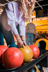 smiling blonde girl choosing bowling ball in bowling club