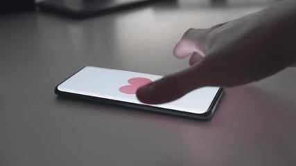 Close-up of Smartphone with Red Heart Appearing on White Screen. Man Waits for the Phone to Find a Date and Picks it Up. Concept of Online Mating