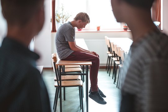 Sad teenage boy sitting alone at school, bullying among children concept