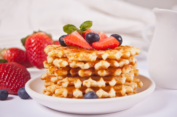 Plate with sweet tasty waffles with honey and berries. Cup of tea and teapot on the background.