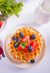 Plate with sweet tasty waffles with honey, berries, cup of tea on the white background.