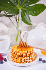 Plate with sweet tasty waffles with honey, berries, cup of tea on the white background.