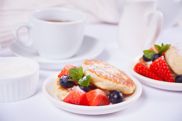 Cottage cheese pancakes, syrniki with berries and powdered sugar. Cup of tea, teapot and jug of milk on the background.