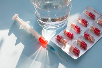Tablets in blister pack, syringe with vaccine and glass of water on grey background.