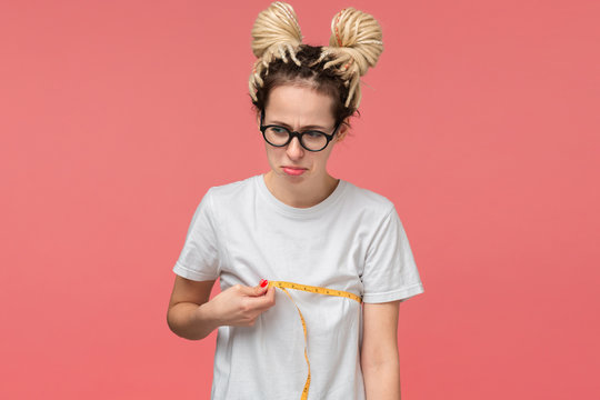 Girl with dreads in a white shirt and glasses looking is upset measuring her boobs