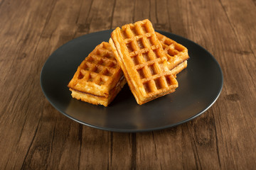 Belgian waffles in a saucer on a wooden table. 