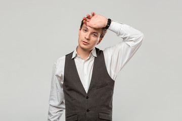 Tired young businessman in a white shirt and grey vest isolated over grey background
