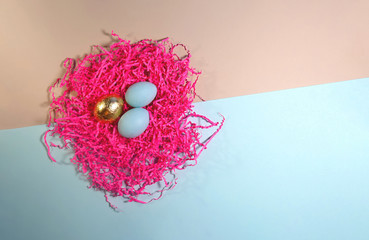 Flat style golden and blue Easter egg in a pink nest on a blue and beige background.