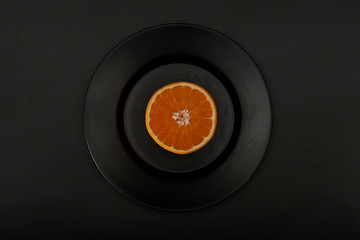 Fresh ripe orange on a black plate on a black background. View from above.