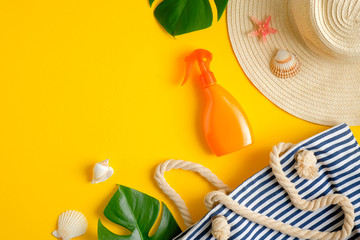 Sunscreen spray bottle, female hat and striped beach bag, tropical leaf on yellow background. Top view, flat lay. Sun protection cosmetic product concept