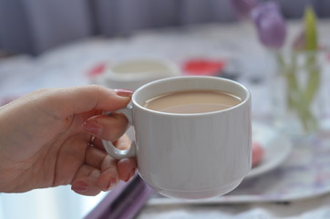 girl holds a cup of coffee tray with paper sketchbook, smartphone and spring flowers on pink bedding. Relaxing, or working, or writing diary or blog in bed at home. with tablet
