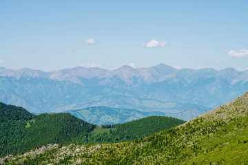 Scenic aerial view to green forest hills and long mountain range under blue sky. Awesome minimalist alpine landscape of vast expanses. Wonderful vivid highland scenery with great mountains and forest.