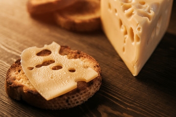 .A slice of sweaty cheese and fried bread on a wooden table. Cheese with big holes. Cheese sandwich.
