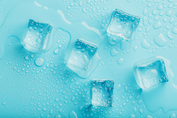 Ice cubes with water drops scattered on a blue background, top view.