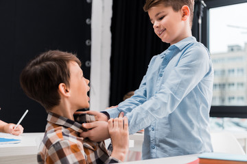 selective focus of cruel schoolkid smiling while bullying classmate