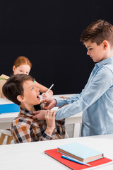 selective focus of cruel schoolboy bullying classmate at school isolated on black