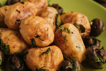 Golden baked potatoes and fried champignons on a green plate on a wooden table. Potatoes with mushrooms.