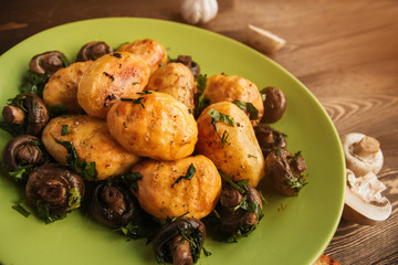 Golden baked potatoes and fried champignons on a green plate on a wooden table. Potatoes with mushrooms.
