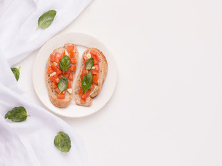 Bruschetta is a traditional Italian dish with tomato, garlic on a plate next to a cloth and basil leaves. copy space