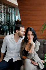Fototapeta premium Business love. Fashionable adult couple. Man in a white shirt and woman in brown suit. They sitting on sofa.