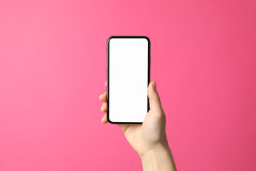 Fototapeta na wymiar Female hand holds phone on pink background. Empty screen