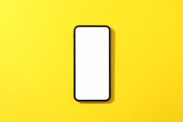 Phone with empty screen on yellow background, top view