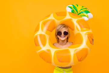 Handsome boy in swimming trunks holds a rubber ring, smiles and gesticulates isolated on orange...