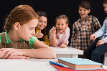 selective focus of upset schoolkid sitting near classmates laughing and pointing with fingers...