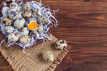Quail eggs are placed in a wicker basket next to a willow twig. Getting ready for Easter. On a wooden background.
