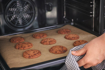 Person taking out baked homemade chocolate chip cookies from oven.