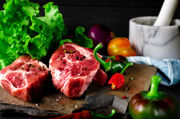 Two juicy steaks lie on a wild stone next to red and green chili peppers and a fresh green salad on a black wooden table