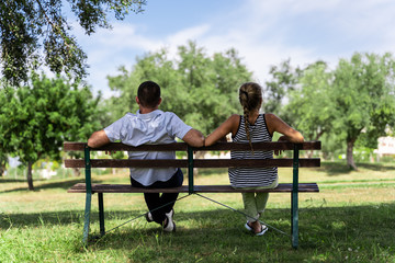 Couple sitting on a wooden bench under a tree looking forward