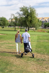 Young couple walking hand in hand on a golf course with a cart