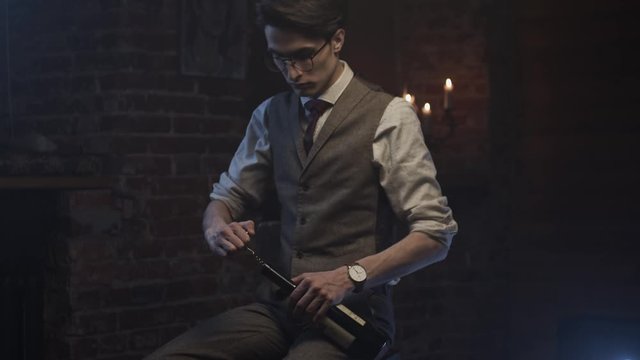 Young man in classic suit opens bottle of red wine, slow motion