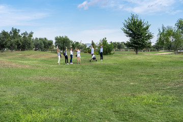 Group of young people on a golf course waving with a cart to transport the equipment