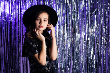 close-up of a stylish girl in a glamorous image with a black hat with brim on a purple tinsel...