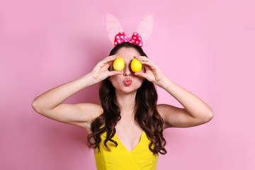 Studio portrait of young beautiful woman wearing traditional bunny ears headband for easter and smiling. Brunette female with wavy hair over yellow background. Close up, copy space.