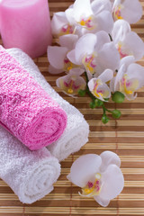 Spa setting with towel, shells, aromatic oil, orchid and candle.