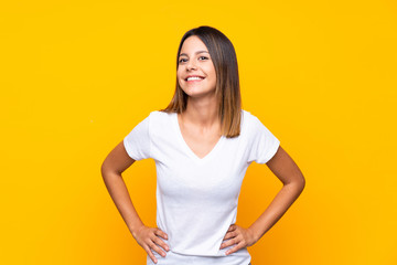 Young woman over isolated yellow background posing with arms at hip and smiling