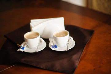 Two cups of espresso on rustic wooden table. Napkins , sugar, spoons on a table.