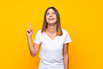 Young woman over isolated yellow background pointing up and surprised