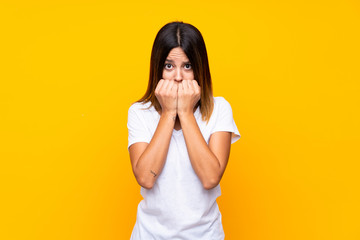 Young woman over isolated yellow background nervous and scared putting hands to mouth