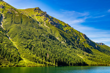 Morskie Oko mountain lake, surrounding forest, Miedziane and Opalony Wierch peaks in background in Tatra Mountains in Poland - obrazy, fototapety, plakaty