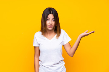 Young woman over isolated yellow background making doubts gesture