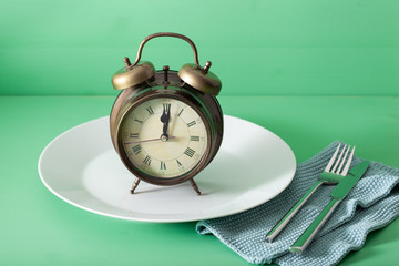 concept of intermittent fasting, ketogenic diet, weight loss. fork and knife on a plate and alarmclock