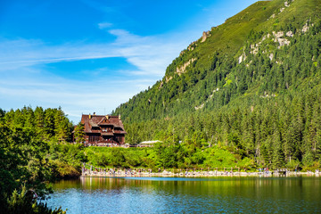 Panoramic view of the Morskie Oko mountain lake surrounding larch, pine and spruce forest with Schronisko przy Morskim Oku shelter house in background © Art Media Factory