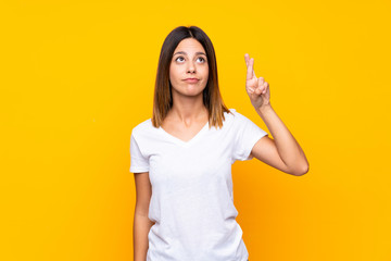 Young woman over isolated yellow background with fingers crossing and wishing the best