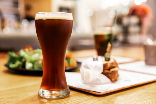 Stout (Black Beer) with froth in drinking glass on a wooden table with blur food in the background.